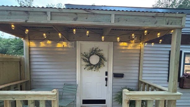 A wooden porch with a white door, a wreath, and string lights. - The Center Street Studio - Sleeps 4 (Searcy)