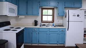 A kitchen with blue cabinets, a white stove, a microwave, a refrigerator, and a window. - The Center Street Studio - Sleeps 4 (Searcy)
