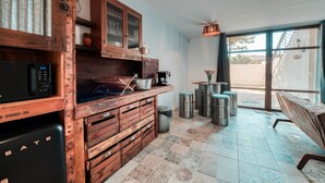 Eine Küche mit Holzsäulen, einer Mikrowelle und einer Kaffeemaschine. In der Nähe des Fensters befinden sich Hocker und eine Bank.
