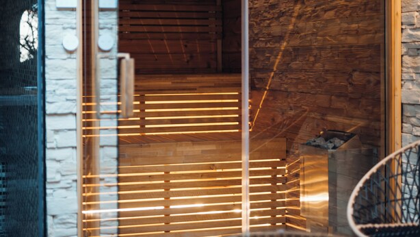 Ein modernes Interieur mit einer Steinwand, Holzboden und einer Glastür zum Saunabereich.
