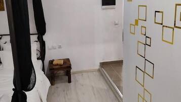 Een slaapkamer met een bed, een klein houten krukje, een witte stoel en een muur met geometrische patronen.