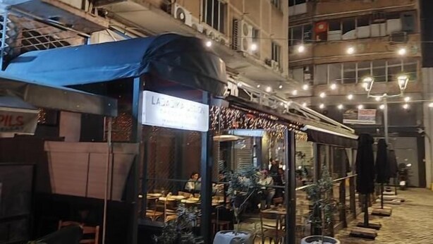 An outdoor café with tables and chairs, potted plants, and a blue awning. - Anchor Suites (Thessaloniki)