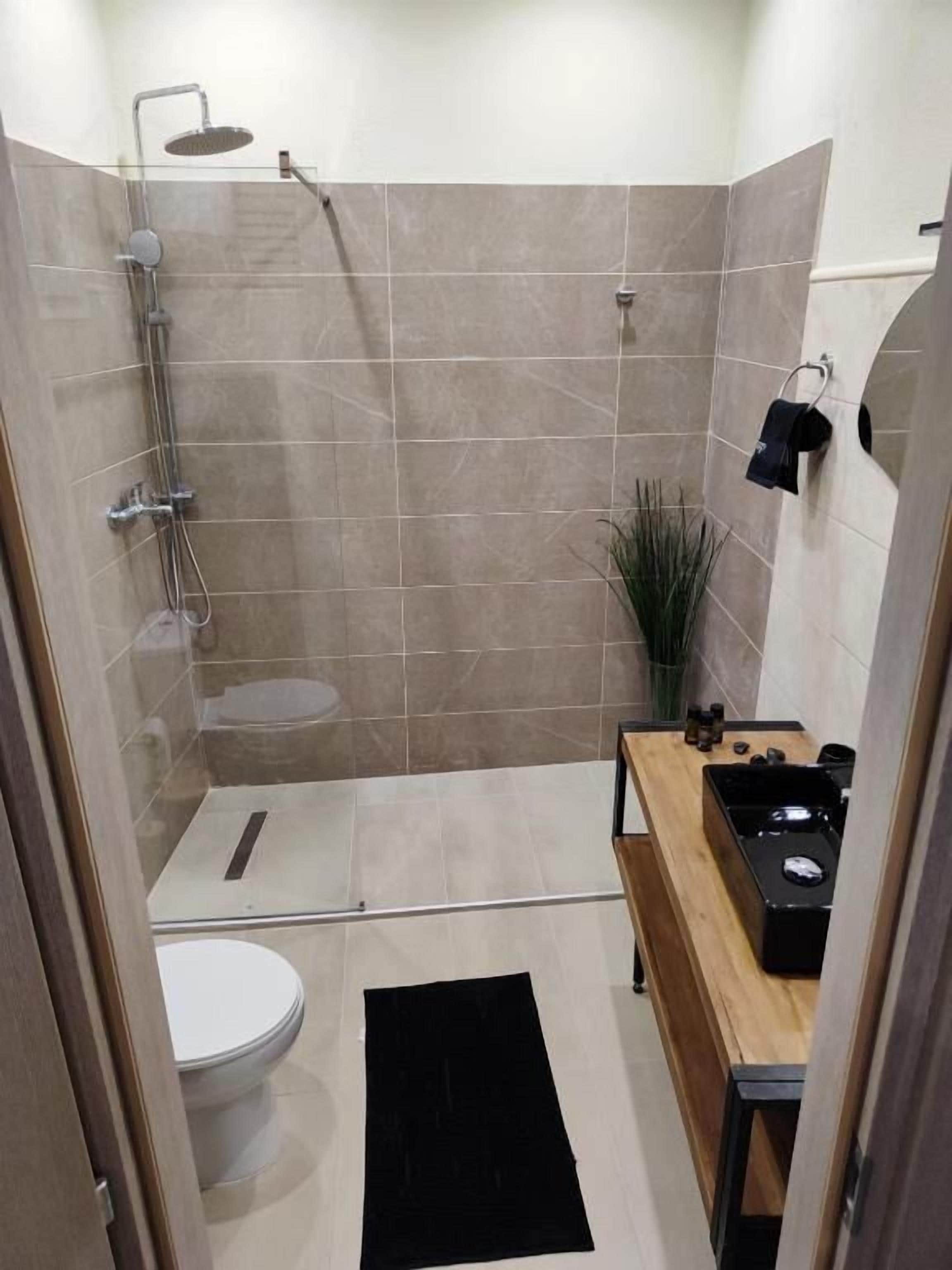 Een kleine badkamer met een douchecabine van glas, een toilet en een houten wastafelmeubel met een wastafel.