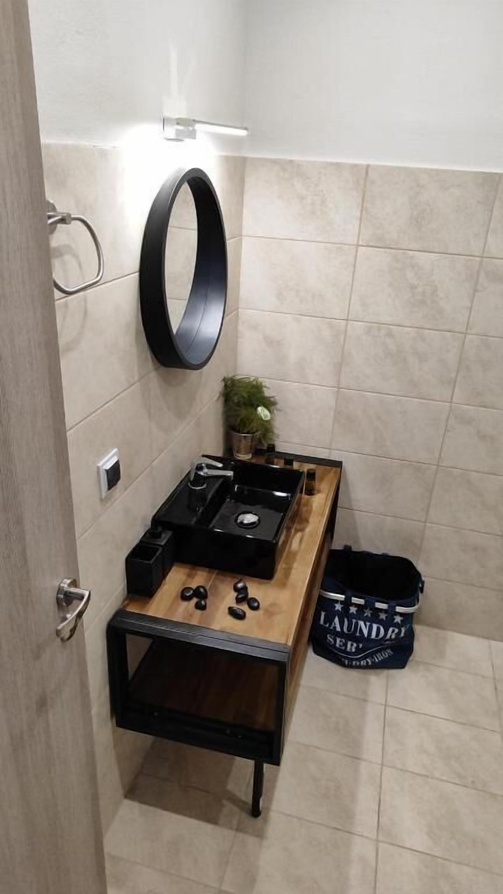 A compact bathroom with a wooden vanity, a black sink, a mirror, and a small potted plant.