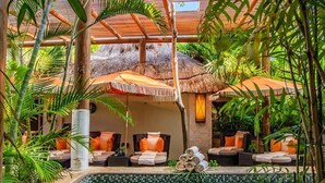 Zona de piscina con sillones de descanso, una estructura de techo de paja y plantas tropicales.
