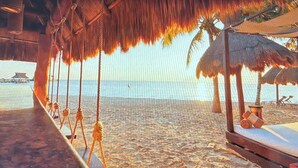 Una playa con sombrillas de paja y una cubierta de madera.