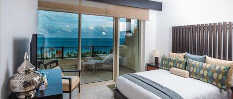Habitación de hotel moderna con una cama grande, un escritorio y vistas al océano a través de un ventanal corredero.