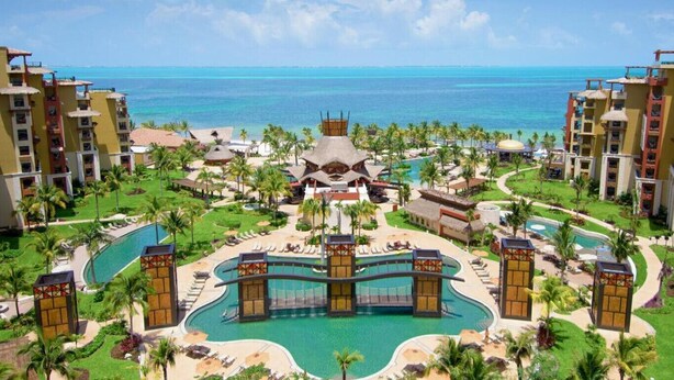 Un resort con varias piscinas, palmeras y vista al océano.