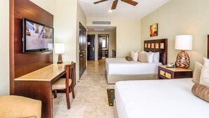 Una habitación de hotel con escritorio, dos camas, televisor y ventilador de techo.