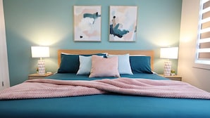 A bedroom with a large bed, two bedside tables, and abstract wall art.