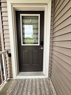 A dark gray front door with a small window above it, a white doorbell, and a textured doormat at the entrance.