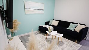 A modern living room with a black sofa, white coffee table, and a painting on the wall.