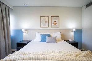 A hotel room with a bed, two bedside tables, a nightstand, a lamp, and two framed artworks on the wall. - Suíte na Berrini by Conviva (Sao Paulo)