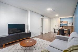 A modern living room with a sofa, a coffee table, a TV, and a dining area with chairs and a table. - Suíte na Berrini by Conviva (Sao Paulo)