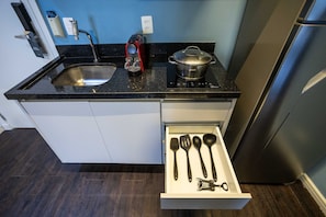 A kitchen with a sink, a red kettle, a pot on the stove, and a drawer with kitchen utensils. - Suíte na Berrini by Conviva (Sao Paulo)