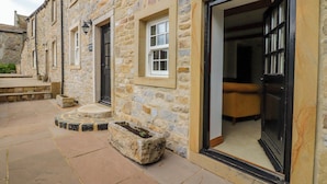 A stone building with a large open doorway, a small window, and a stone planter. - Rowan Tree Cottage (Skipton)