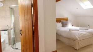 A bedroom with a large bed, a headboard, and a skylight. - Rowan Tree Cottage (Skipton)