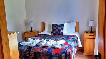 Une chambre à coucher avec un lit en bois, une courtepointe aux couleurs vives, deux tables de chevet avec des lampes et un plafond en bois.