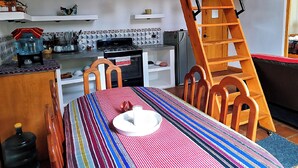 Une cuisine avec une échelle en bois, une table recouverte d’une nappe à rayures et un poêle.