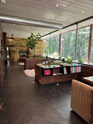 Un interior moderno con pared de piedra, chimenea, ventanas amplias y una zona de estar.