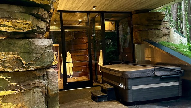 A modern outdoor bathroom with a stone wall, a wooden bench, and a mattress.