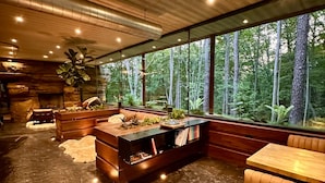 A modern interior with a stone fireplace, wooden furniture, and a view of a forest through large windows.