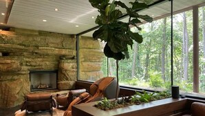 A modern interior with a stone wall, leather furniture, a fireplace, and a large window with a forest view.