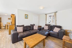 A living room with a dark leather sectional sofa, a wooden coffee table, and a dining area with a wooden table and chairs. - Host Stay Easton Meadows Holiday Cottage (Bridlington)