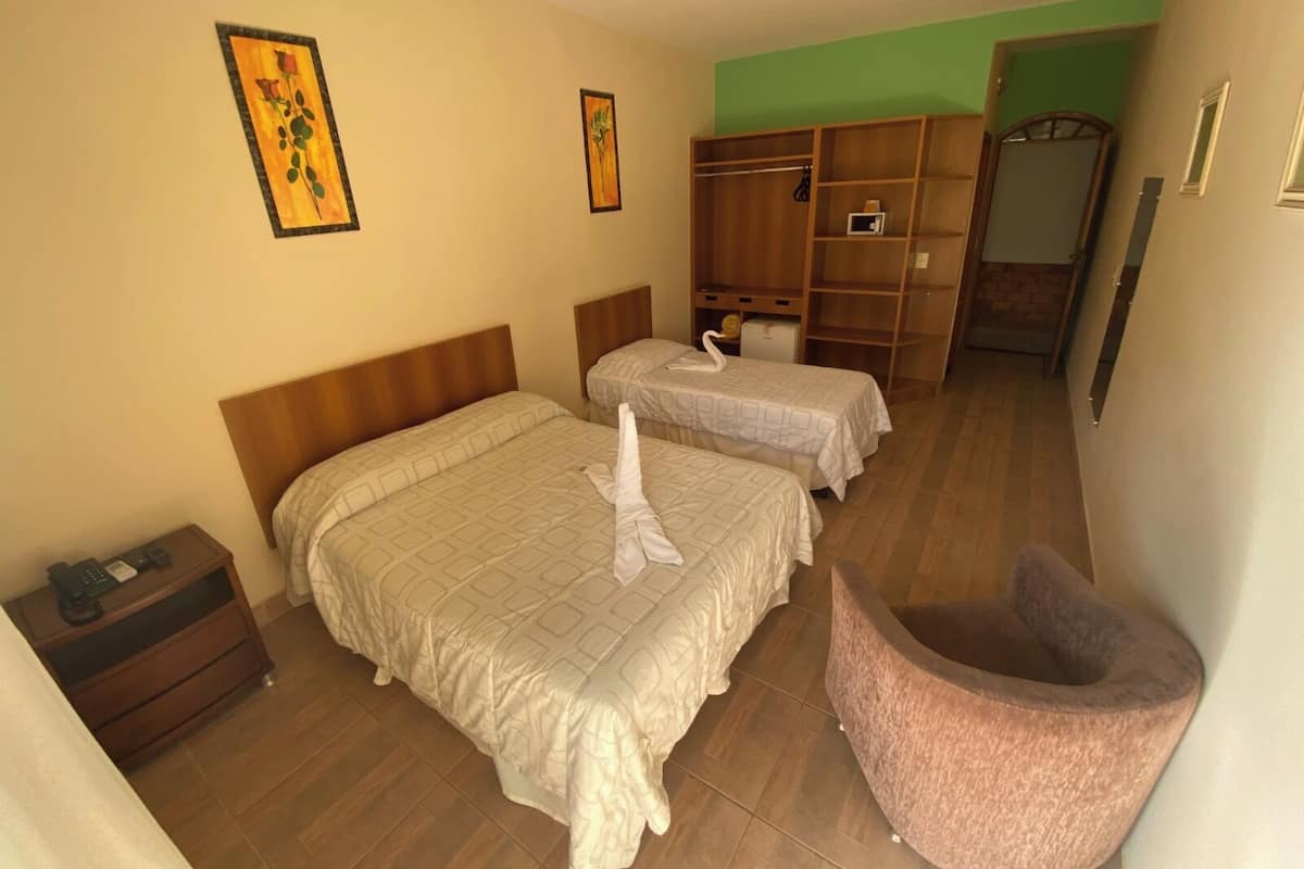 Een hotelkamer met twee bedden, een houten garderobe, een klein bureau met een telefoon en een roze stoel.