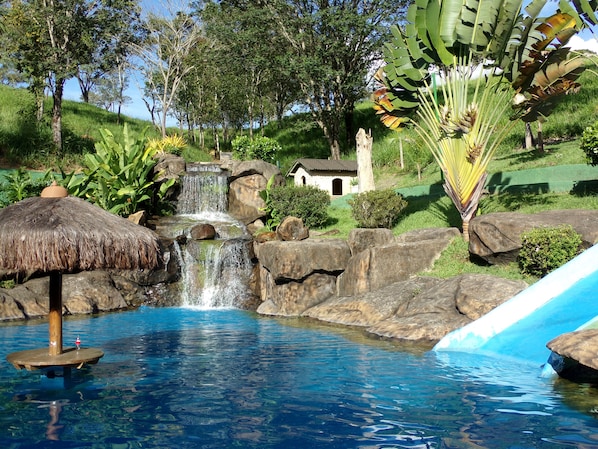 Una piscina cristalina con una cascada, rodeada de rocas y vegetación.