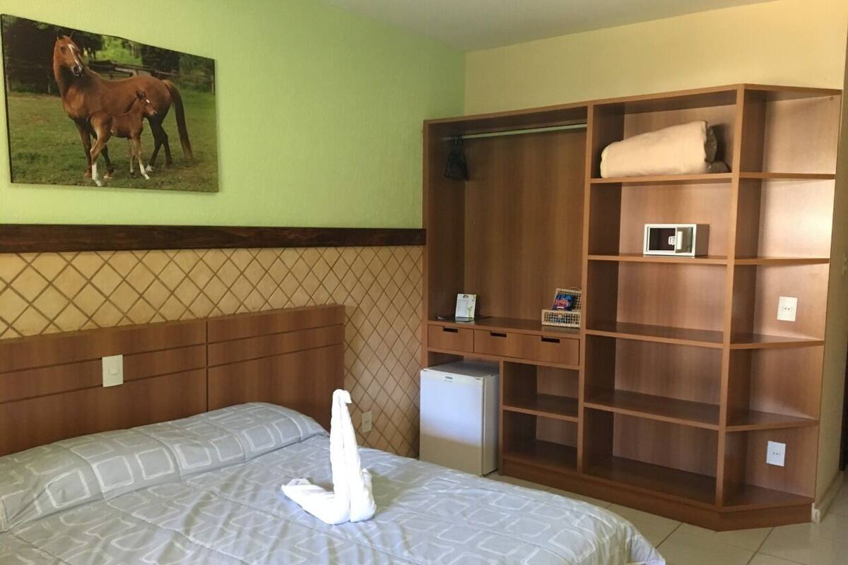 Een hotelkamer met een bed, een houten kledingkast, een kleine koelkast en een wandplank.