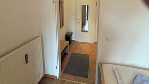 A hallway leading to a bathroom with a mirror, a radiator, and a bench.