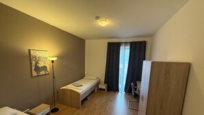 A hotel room with a bed, a desk, a chair, a wardrobe, a lamp, and a painting on the wall.