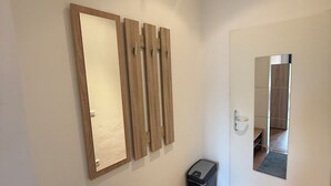 A hallway with a wooden bench, a trash bin, and a door with a mirror.