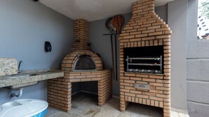 Una cocina exterior de ladrillo con horno de pizza y parrilla, un lavadero y un cubo de basura.