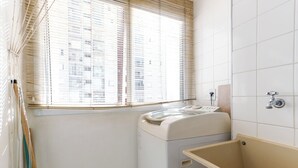 Un lavadero con lavadora, bañera y ventana con persianas.