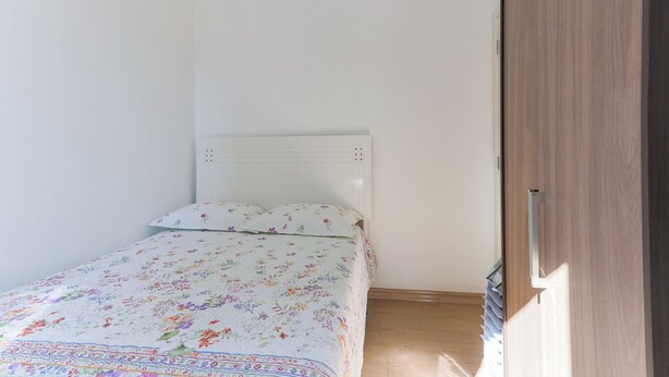 Un dormitorio pequeño y ordenado con una cama individual, un armario de madera y un cabecero blanco.