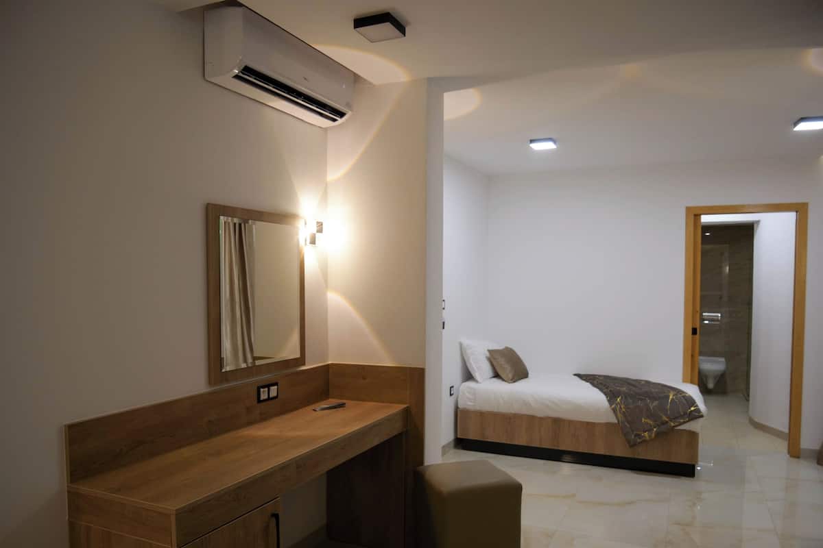 A modern bedroom with a wooden vanity, a bed with a blanket, and a bathroom visible through an open door.