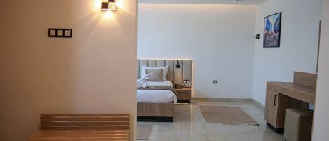 A modern hotel room with a wooden bench, a bed with a headboard, a nightstand, and a desk.