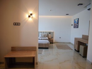 A modern hotel room with a wooden bench, a bed with a headboard, a nightstand, and a desk.