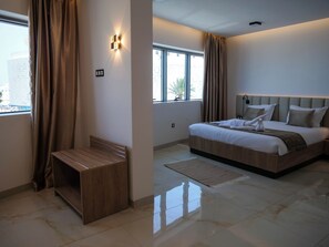 A modern hotel room with a large bed, a wooden bench, and a view of the city through the window.