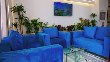 A reception area with blue sofas, a glass coffee table, and various plants.