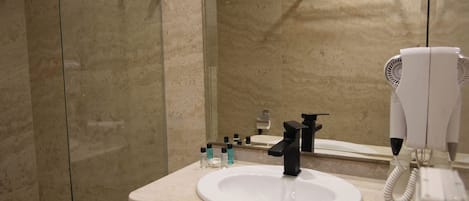 Un baño moderno con cabina de ducha de vidrio, un lavabo blanco y un secador de pelo.
