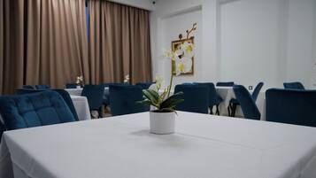 A conference room with a white table, blue chairs, a potted orchid, and brown curtains.