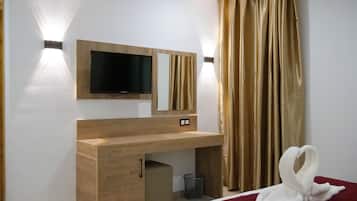 A hotel room with a wooden desk, a flat-screen TV mounted above it, a bed with a red blanket, and a golden curtain.