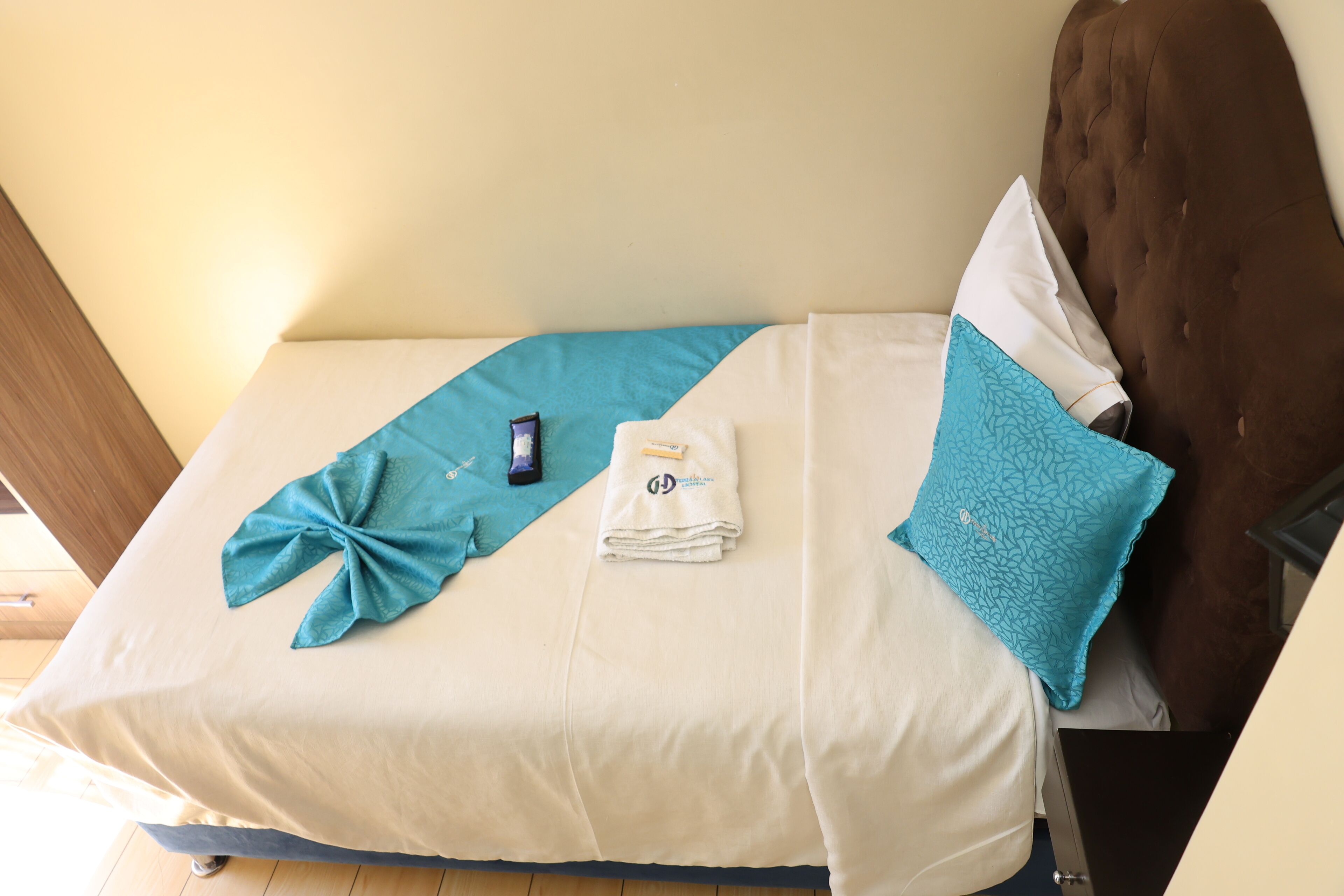 Una cama bien hecha con una colcha azul y blanca, una toalla doblada y un teléfono inteligente sobre la cama.