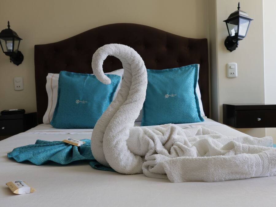 Una cama bien hecha con una toalla con forma de cisne y almohadas color turquesa.