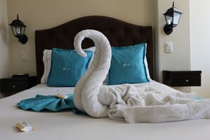 Una cama bien hecha con una toalla con forma de cisne y almohadas color turquesa.