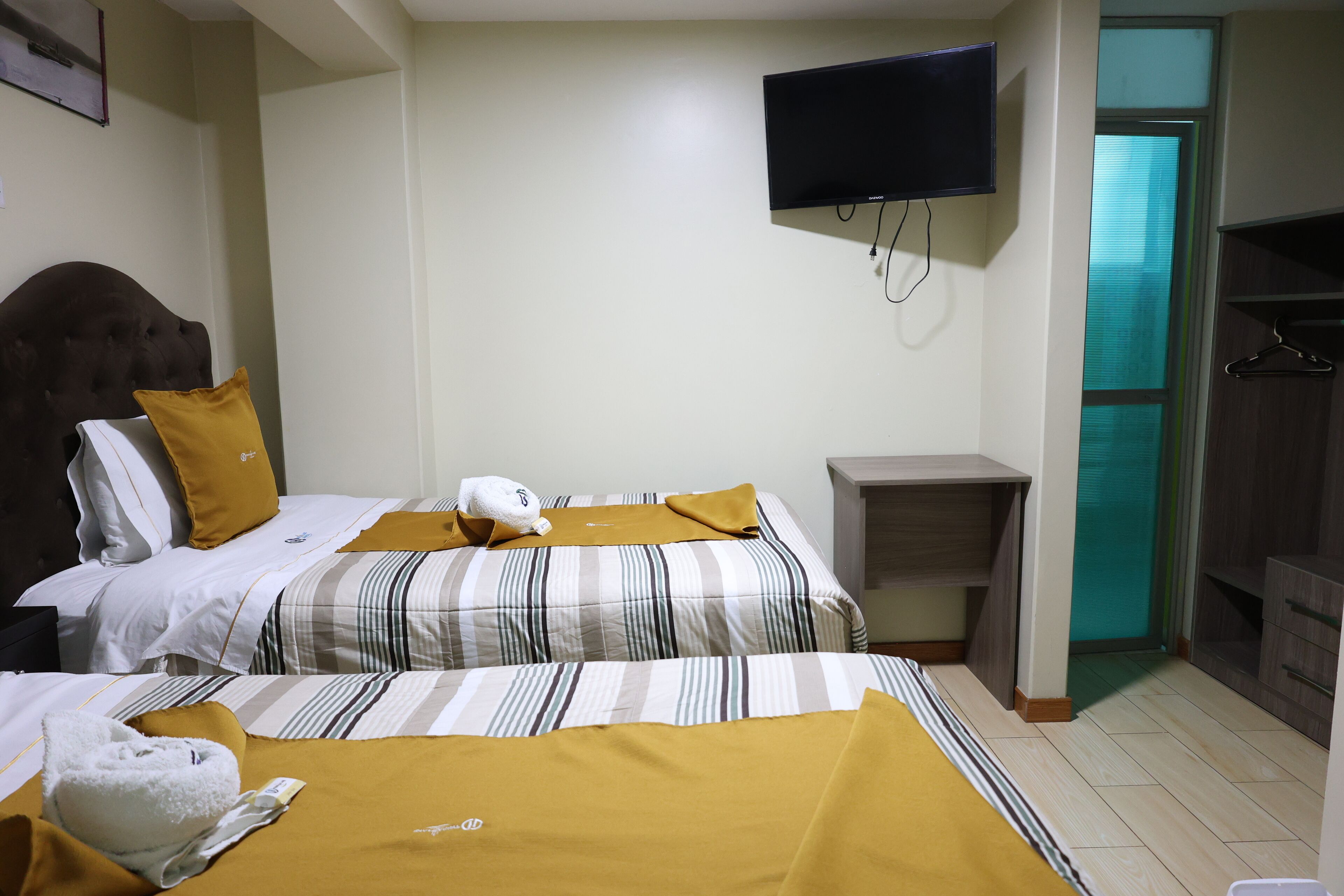 Habitación de hotel con dos camas, televisión montada en la pared, un escritorio pequeño y un armario.