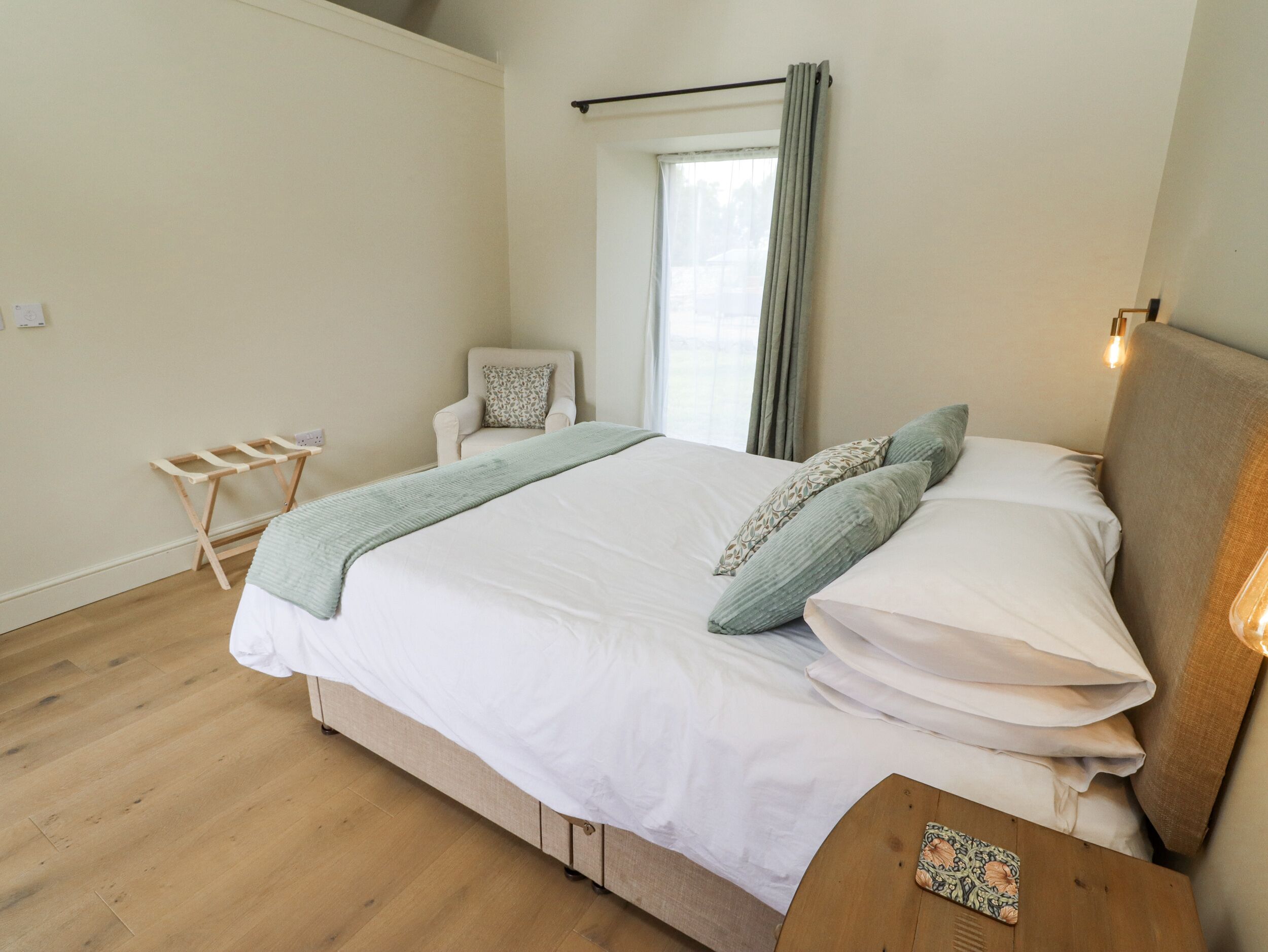 Un dormitorio con cama, una silla, un tendedero de madera y una mesita de noche con lámpara.